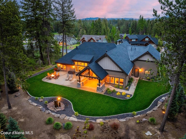 11671 N Spiraea Ln, Hayden, ID 83835 - back of property at dusk featuring a fire pit, board and batten siding, a patio area, a lawn, and roof with shingles