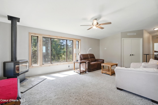 living area with a ceiling fan, carpet, visible vents, vaulted ceiling, and a wood stove