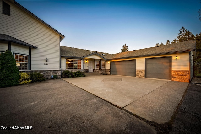 view of front of house with stone siding, driveway, an attached garage, and roof with shingles