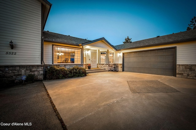 view of front of house with stone siding, concrete driveway, an attached garage, and a porch