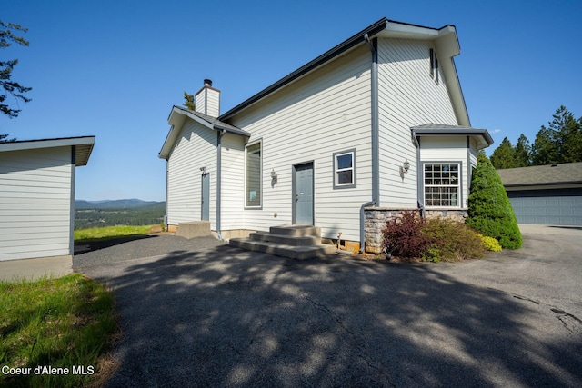 back of house featuring a chimney, a mountain view, and stone siding