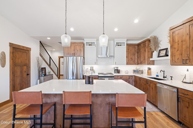 kitchen featuring appliances with stainless steel finishes, a sink, wall chimney exhaust hood, backsplash, and a kitchen island