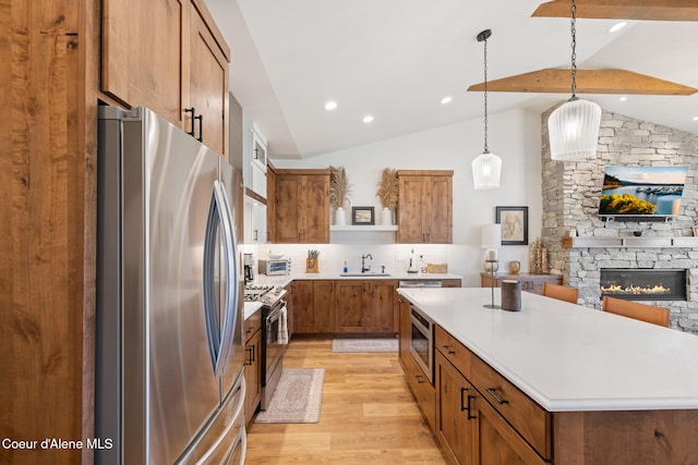 kitchen featuring appliances with stainless steel finishes, a sink, lofted ceiling, brown cabinets, and light wood-type flooring