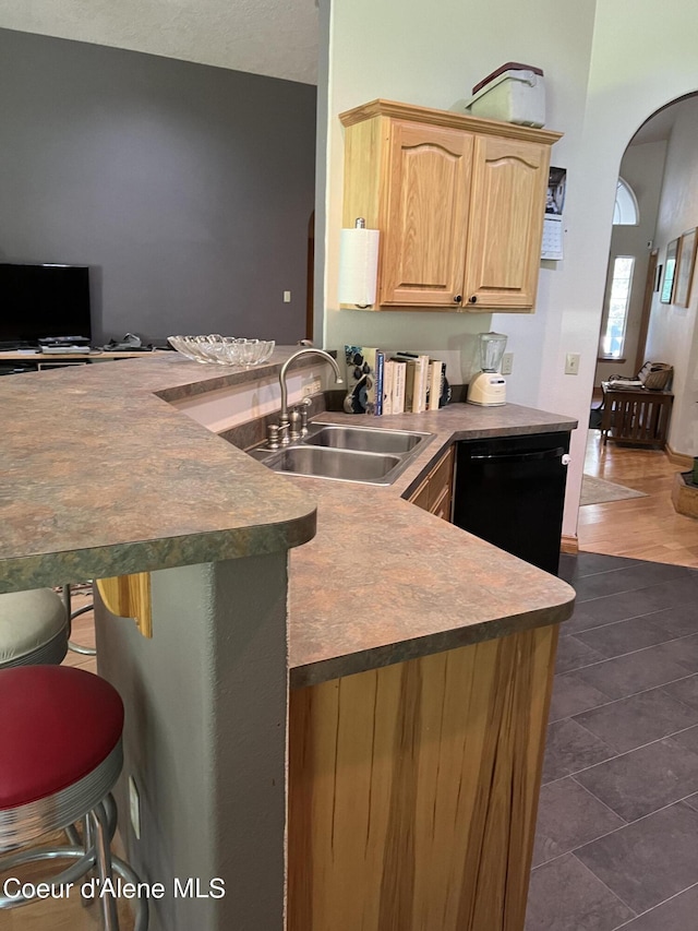 kitchen with a peninsula, light brown cabinetry, a sink, arched walkways, and dishwasher