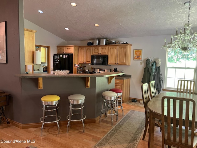kitchen with light wood-style flooring, a kitchen breakfast bar, a textured ceiling, baseboards, and black appliances
