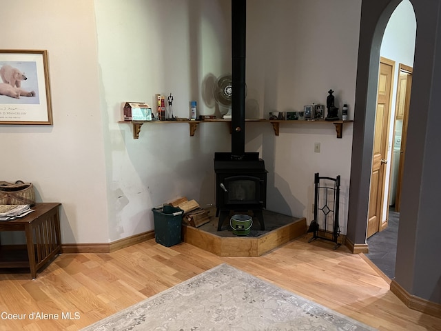 living room featuring a wood stove, wood finished floors, baseboards, and arched walkways