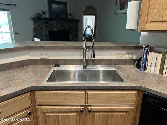kitchen with dark countertops, black dishwasher, a fireplace, and a sink