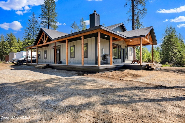 rear view of property with a chimney, board and batten siding, a porch, and a shingled roof