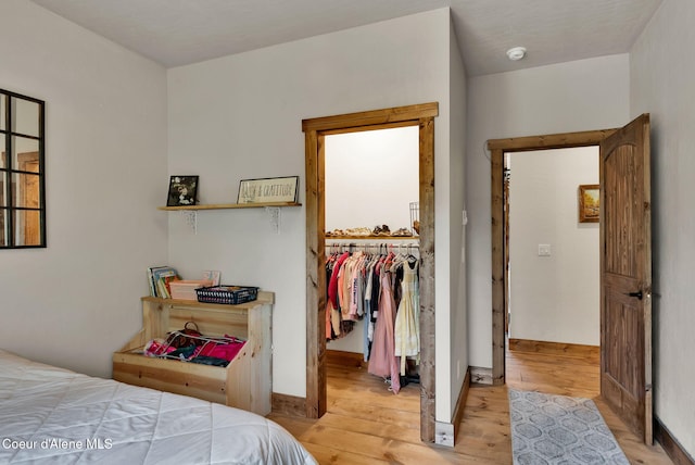bedroom with baseboards, light wood-style floors, and a spacious closet