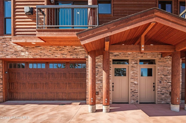 entrance to property with concrete driveway, stone siding, and a balcony