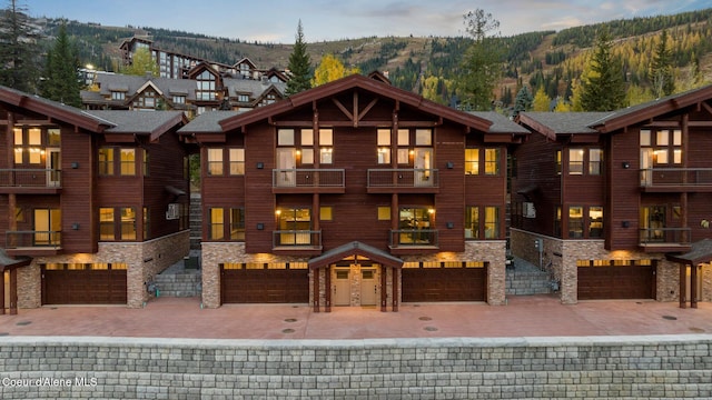 townhome / multi-family property featuring a balcony, driveway, a mountain view, an attached garage, and stone siding