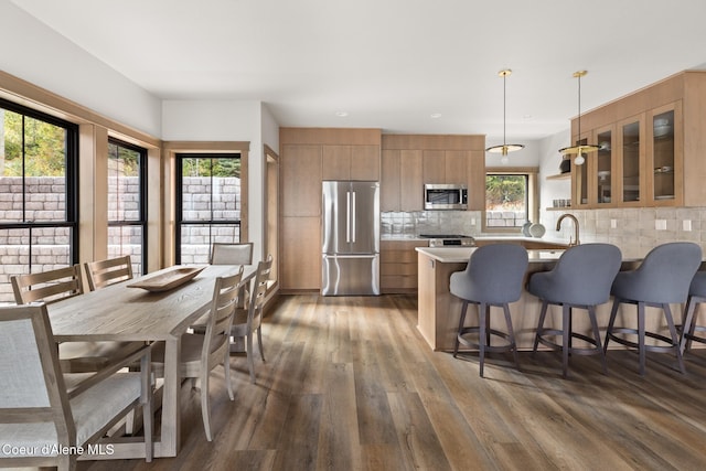 kitchen featuring stainless steel appliances, brown cabinets, a kitchen breakfast bar, dark wood finished floors, and glass insert cabinets