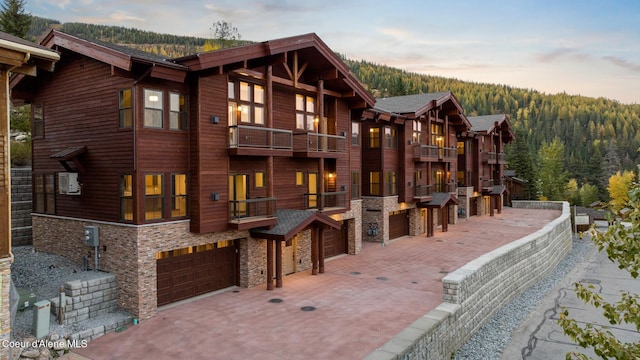 exterior space with stone siding, a forest view, a garage, and a balcony