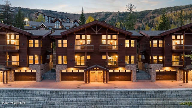 multi unit property with stone siding, a mountain view, a garage, a balcony, and driveway