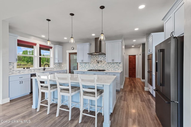kitchen with stainless steel appliances, wall chimney range hood, decorative backsplash, light countertops, and wood finished floors