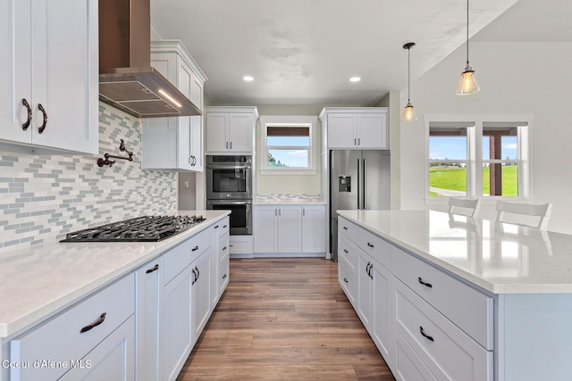 kitchen with appliances with stainless steel finishes, wall chimney range hood, tasteful backsplash, white cabinets, and recessed lighting