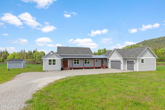 view of front of house with gravel driveway, an outdoor structure, a porch, a front lawn, and an attached garage