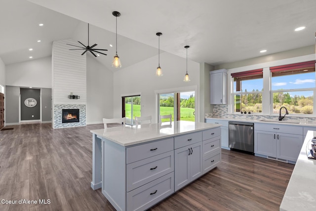 kitchen featuring stainless steel dishwasher, a sink, dark wood-type flooring, a center island, and decorative light fixtures