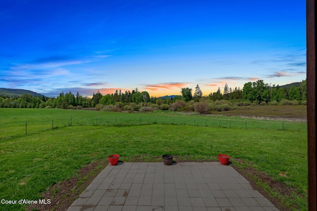 yard at dusk featuring a view of countryside and a patio