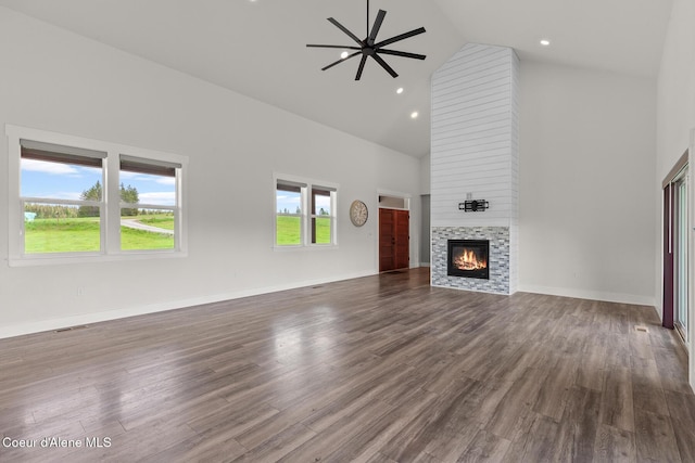 unfurnished living room with high vaulted ceiling, ceiling fan, a tiled fireplace, dark wood-style flooring, and baseboards