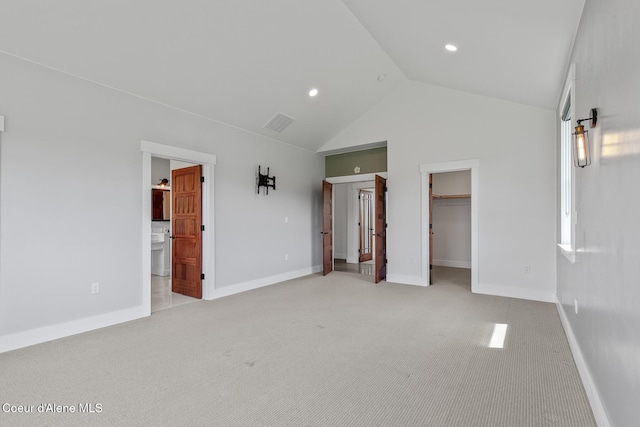 unfurnished bedroom featuring light carpet, lofted ceiling, a spacious closet, and baseboards