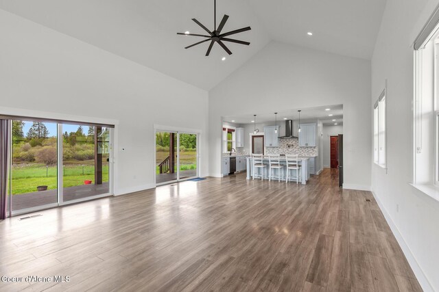 unfurnished living room with high vaulted ceiling, ceiling fan, wood finished floors, recessed lighting, and baseboards