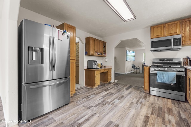 1729 N 9th St, Coeur Dalene, ID 83814 - kitchen with stainless steel appliances, light wood-style floors, arched walkways, brown cabinets, and baseboards