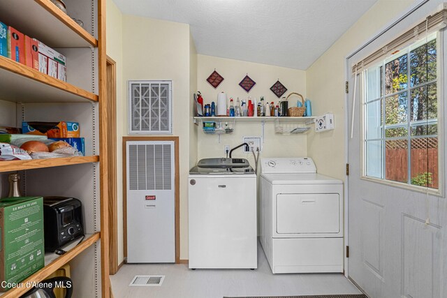 laundry area with a heating unit, washer and dryer, a textured ceiling, and light flooring