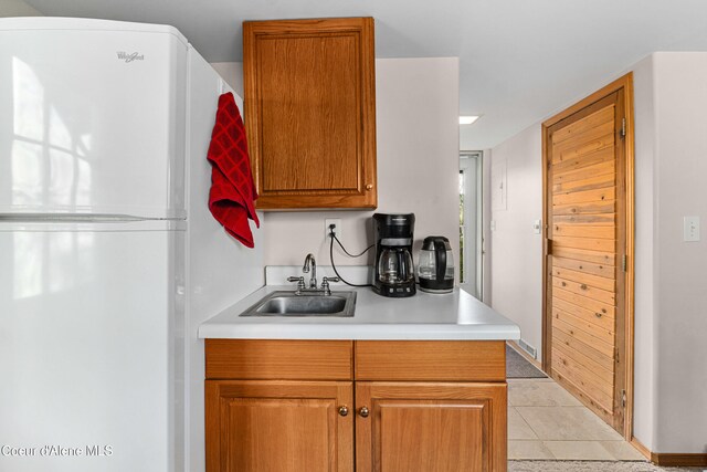 kitchen featuring freestanding refrigerator, a sink, light countertops, brown cabinetry, and tile patterned floors