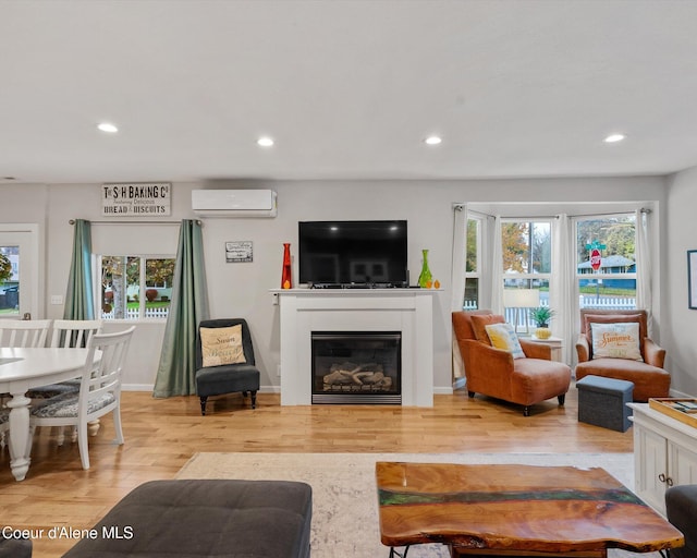 living room with a wall mounted air conditioner, recessed lighting, light wood-type flooring, plenty of natural light, and a glass covered fireplace