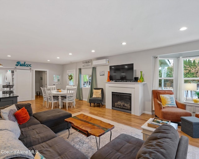 living area with an AC wall unit, recessed lighting, light wood-style flooring, and a glass covered fireplace