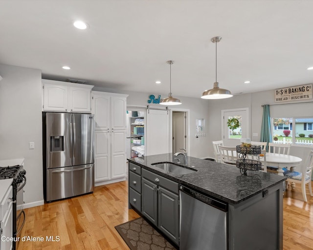 kitchen with stainless steel appliances, a sink, white cabinets, light wood finished floors, and an island with sink