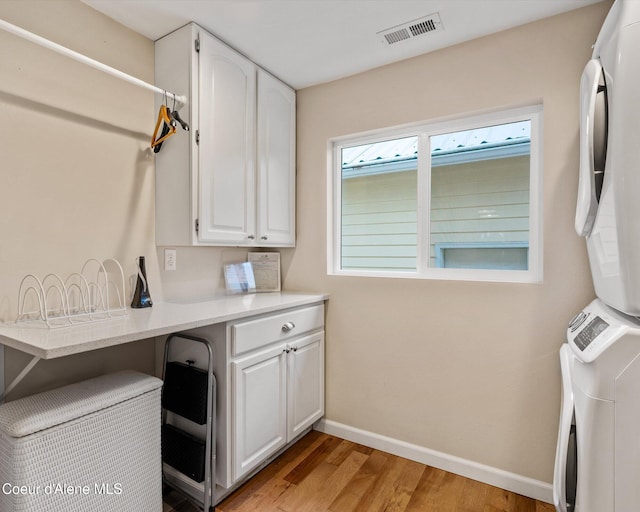 washroom with stacked washer and clothes dryer, cabinet space, light wood-type flooring, and baseboards