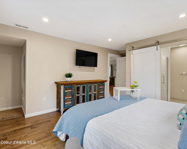 bedroom featuring wood finished floors, a barn door, baseboards, and recessed lighting