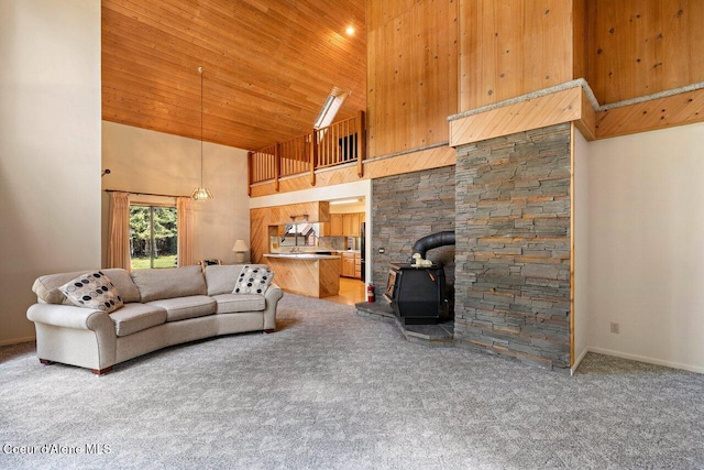 living area featuring high vaulted ceiling, a wood stove, carpet, wood ceiling, and baseboards
