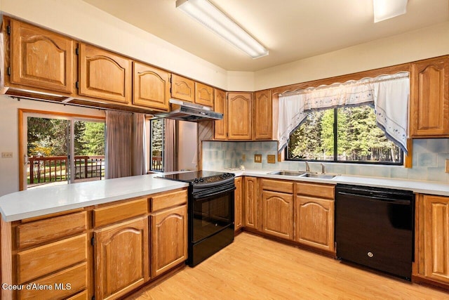 kitchen with black appliances, a sink, a peninsula, brown cabinetry, and light wood finished floors