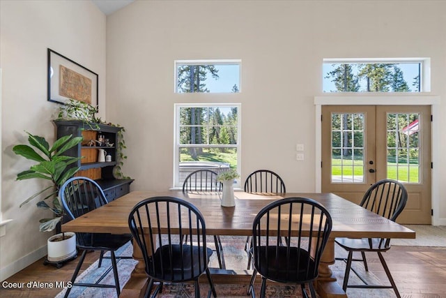dining space featuring a towering ceiling, french doors, wood finished floors, and baseboards