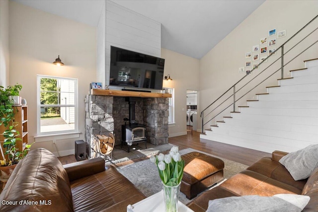 living area with stairs, high vaulted ceiling, wood finished floors, a wood stove, and baseboards