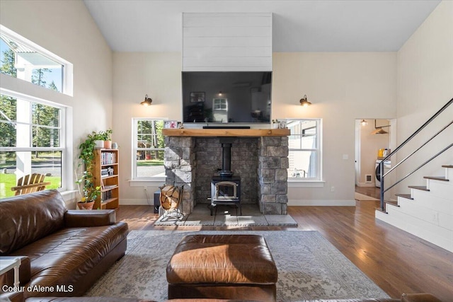 living area featuring a wood stove, a high ceiling, wood finished floors, baseboards, and stairs