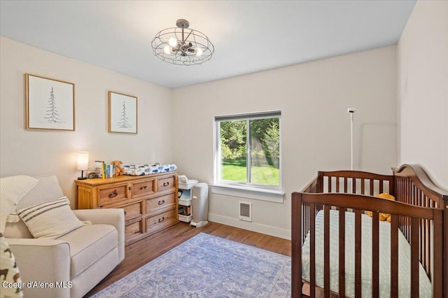 bedroom with a chandelier, baseboards, wood finished floors, and a nursery area