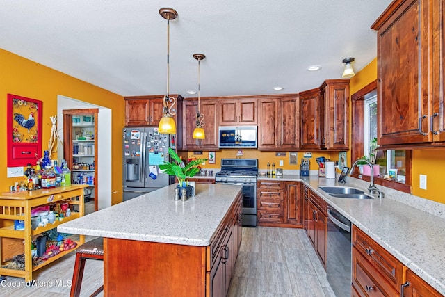 kitchen featuring appliances with stainless steel finishes, a sink, light stone counters, a center island, and decorative light fixtures