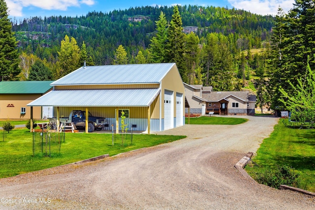 view of front facade featuring a view of trees, a front yard, driveway, and metal roof
