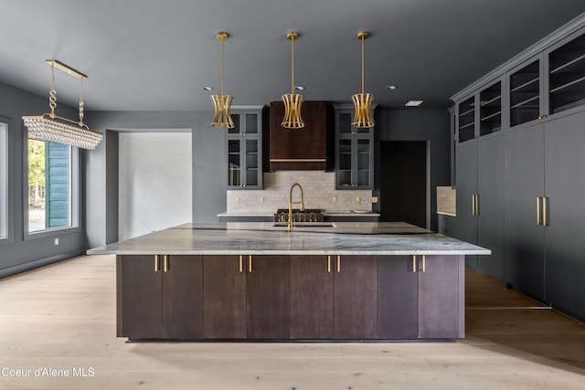 kitchen with tasteful backsplash, glass insert cabinets, dark brown cabinets, a spacious island, and light wood-style floors