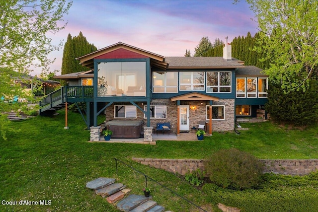 back of house featuring a hot tub, a patio, stone siding, a lawn, and a chimney
