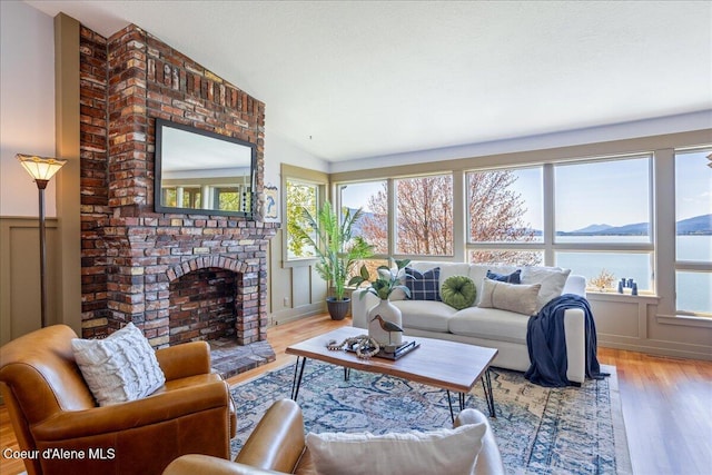 living room with wood finished floors, a fireplace, vaulted ceiling, a decorative wall, and wainscoting