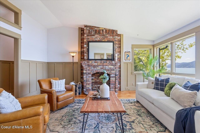 living area with lofted ceiling, a wainscoted wall, wood finished floors, a fireplace, and a decorative wall