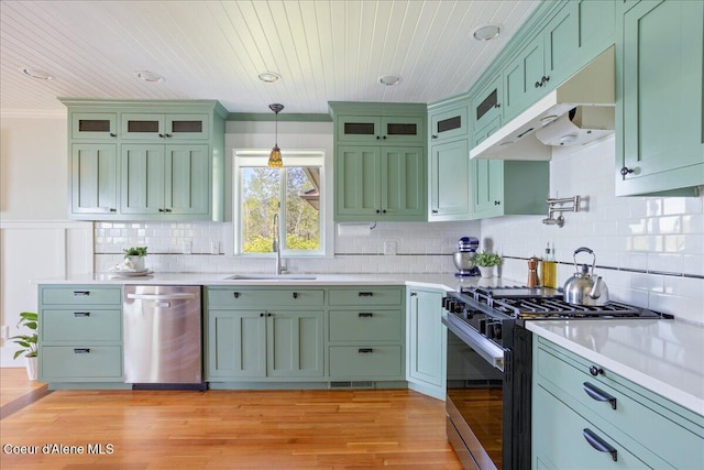 kitchen featuring dishwasher, black gas stove, under cabinet range hood, green cabinets, and a sink