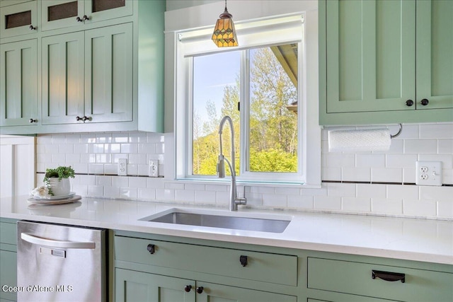 kitchen featuring stainless steel dishwasher, green cabinets, a sink, and decorative backsplash