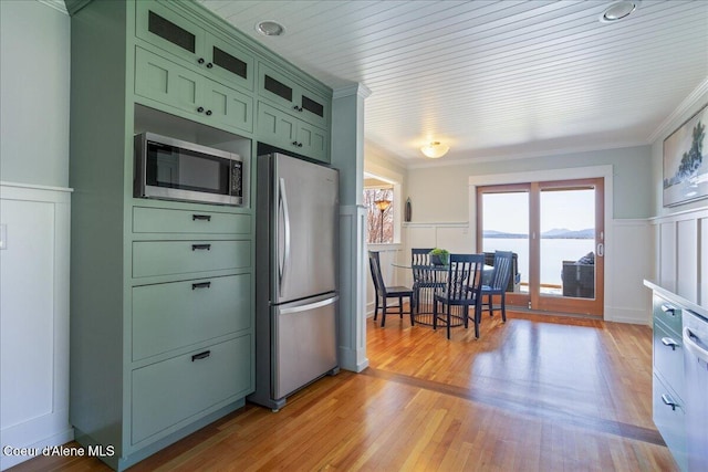 kitchen with green cabinets, stainless steel appliances, a wainscoted wall, a decorative wall, and ornamental molding