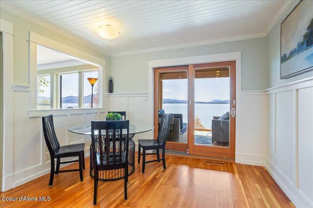 dining room with a decorative wall, plenty of natural light, wood finished floors, wainscoting, and crown molding